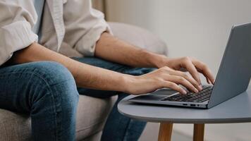 Close-up male hands typing on laptop keyboard. Unrecognizable guy unknown business man in jeans casual shirt sitting on sofa with computer working chatting e-learning email answer online distant job photo