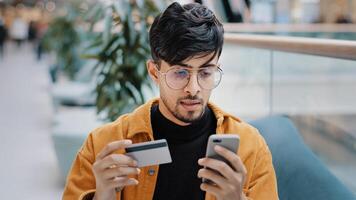 Focused indian man guy customer pay by card on phone using e-banking mobile application arabian male shopper making buying in online store paying purchase use instant easy payment on smartphone photo