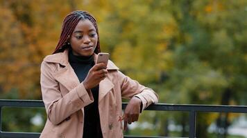 Young serious female standing in autumn park holding mobile phone browsing email remotely communicating in social network using smartphone outdoors searching for information on internet writes sms photo