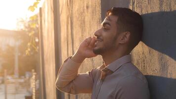 Side view handsome bearded hispanic arabic business man client guy standing near stone wall talking on mobile phone answering call talks with smartphone conversation using wireless cellphone in city photo