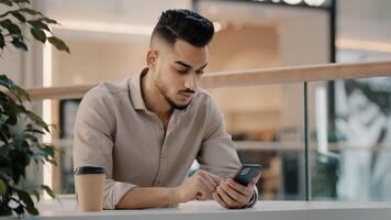 Indian Hispanic man typing smartphone scrolling social media male businessman online message reading news entrepreneur chatting browsing with smartphone using mobile phone in cafe sitting at table photo
