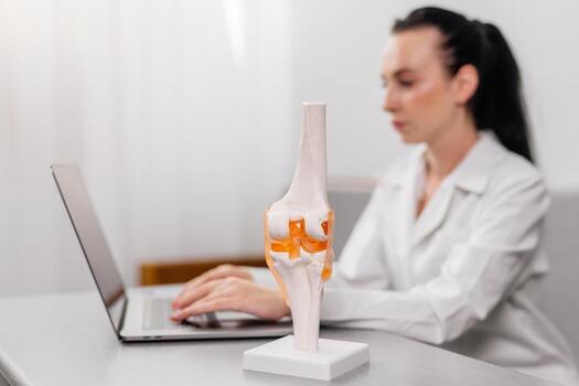 Orthopedic surgeon shows a detailed knee joint model during a medical consultation, demonstrating treatment methods. Ideal for illustrating expert medical advice and advanced orthopedic care photo