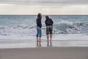 A mother and daughter standing on the beach, looking at the sea, rear view. photo