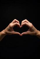 Hands gesture forming heart shape on black background photo