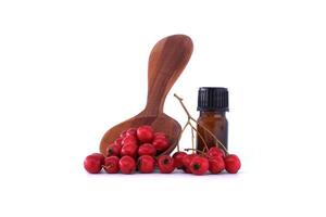 Hawthorn berries and essential oil bottle with wooden spoon isolated on white background photo