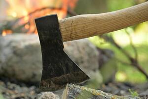 Hatchet lodged in a log of wood, situated opposite a campfire photo