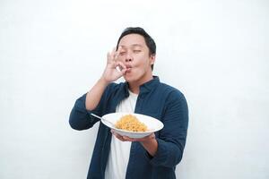 A portrait of happy Asian man wearing a blue shirt while holding a plate of fried noodles. Young man smiling and pointing to a plate of noodle. Isolated with a white background. photo