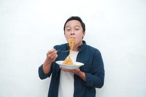 A portrait of happy Asian man wearing a blue shirt while holding a plate of fried noodles. Young man smiling and pointing to a plate of noodle. Isolated with a white background. photo