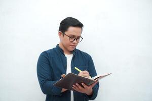 Young Asian man holding a book while thinking and concentrating. Asian student looking for ideas while studying over white background photo