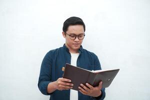 Young Asian man holding a book while thinking and concentrating. Asian student looking for ideas while studying over white background photo