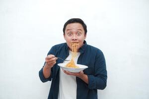 A portrait of happy Asian man wearing a blue shirt excited to eat a plate of fried noodles. Young man smiling and holding a plate of noodle. Isolated with a white background. photo