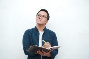 Young Asian man holding a book while thinking and concentrating. Asian student looking for ideas while studying over white background photo