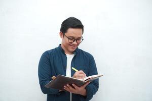 Young Asian man holding a book while thinking and concentrating. Asian student looking for ideas while studying over white background photo
