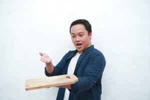 Portrait of happy Asian man holding an empty cutting with happy and excited expression. Young man showing and pointing empty wooden cutting board. Isolated with a white background. photo