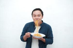 A portrait of happy Asian man wearing a blue shirt excited to eat a plate of fried noodles. Young man smiling and holding a plate of noodle. Isolated with a white background. photo