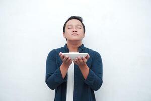 A portrait of happy Asian man wearing a blue shirt excited to eat a plate of fried noodles. Young man smelling the aroma of delicious fried noodles. Isolated with a white background. photo