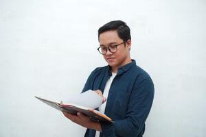 Young Asian man holding a book while thinking and concentrating. Asian student looking for ideas while studying over white background photo