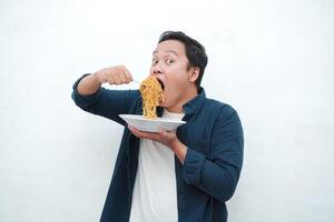 A portrait of happy Asian man wearing a blue shirt excited to eat a plate of fried noodles. Young man smiling and holding a plate of noodle. Isolated with a white background. photo