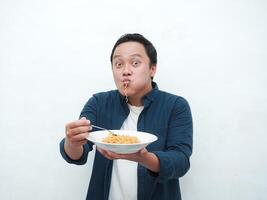 A portrait of happy Asian man wearing a blue shirt while holding a plate of fried noodles. Young man smiling and pointing to a plate of noodle. Isolated with a white background. photo