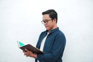 Young Asian man holding a book while thinking and concentrating. Asian student looking for ideas while studying over white background photo
