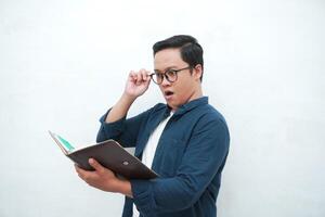 Young Asian man holding a book while thinking and concentrating. Asian student looking for ideas while studying over white background photo