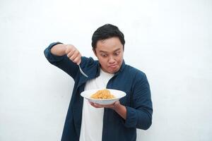 A portrait of happy Asian man wearing a blue shirt while holding a plate of fried noodles. Young man smiling and pointing to a plate of noodle. Isolated with a white background. photo