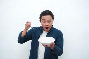 Portrait of happy Asian man wearing a blue shirt while holding an empty plate with happy and excited expression. Young man showing and pointing empty mockup plate. Isolated with a white background. photo