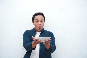 Portrait of happy Asian man wearing a blue shirt while holding an empty plate with happy and excited expression. Young man showing and pointing empty mockup plate. Isolated with a white background. photo