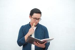 Young Asian man holding a book while thinking and concentrating. Asian student looking for ideas while studying over white background photo