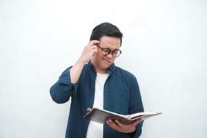 Young Asian man holding a book while thinking and concentrating. Asian student looking for ideas while studying over white background photo