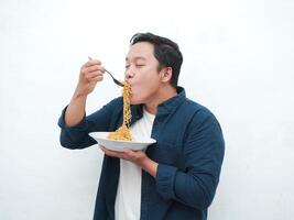 A portrait of happy Asian man wearing a blue shirt while holding a plate of fried noodles. Young man smiling and pointing to a plate of noodle. Isolated with a white background. photo