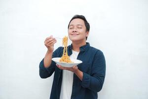 A portrait of happy Asian man wearing a blue shirt excited to eat a plate of fried noodles. Young man smiling and holding a plate of noodle. Isolated with a white background. photo