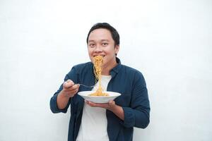 A portrait of happy Asian man wearing a blue shirt excited to eat a plate of fried noodles. Young man smiling and holding a plate of noodle. Isolated with a white background. photo