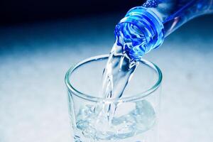 Close-Up of Water Being Poured from a Blue Plastic Bottle into a Glass on a Light Background photo