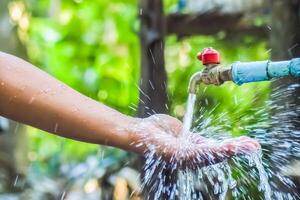 Close-Up of Hand Under Running Water from Outdoor Faucet with Splashing Water Droplets photo