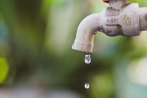 Close-up of a Dripping Water Faucet with Blurred Green Background in Natural Light photo