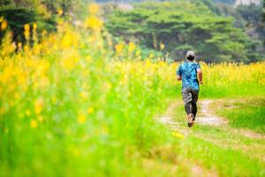 Man Running on a Trail Through a Vibrant Flower Field with Lush Greenery and Trees in the Background photo