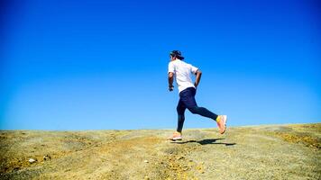 Man Running on Rocky Terrain Under Clear Blue Sky, Outdoor Fitness and Adventure Concept photo