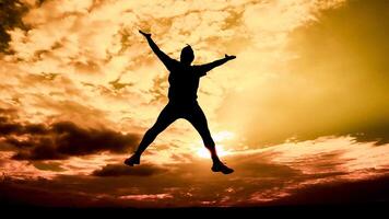 Silhouette of a Person Jumping Against a Vibrant Sunset Sky with Dramatic Clouds photo