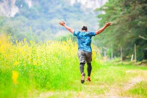 Man Running Joyfully Through a Green Field with Yellow Flowers and Lush Trees in the Background photo