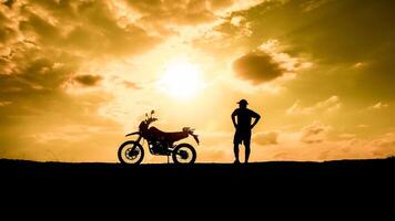 Silhouette of a Man and Motorcycle Against a Golden Sunset Sky with Dramatic Clouds photo