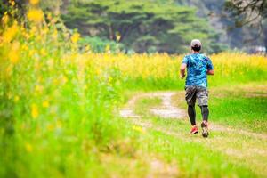 Man Running on a Trail in a Lush Green Field with Yellow Flowers and Trees in the Background photo