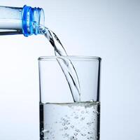 Fresh Water Pouring from Bottle into Glass on White Background with Bubbles and Splash photo