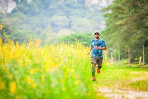 Man Jogging on a Scenic Nature Trail Surrounded by Lush Greenery and Yellow Flowers on a Sunny Day photo