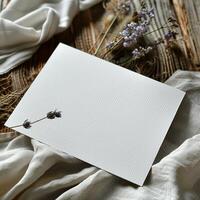 Blank Greeting Card Mockup with Dried Lavender Stems on Rustic Wooden Table and White Fabric. photo