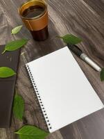 Still life photography blank notebook on wooden table with a cup of coffee, plant, leaf on table photo