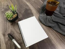 Still life photography blank notebook on wooden table with a cup of coffee, plant, leaf on table photo