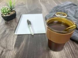 Still life photography blank notebook on wooden table with a cup of coffee, plant, leaf on table photo