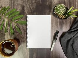 Still life photography blank notebook on wooden table with a cup of coffee, plant, leaf on table photo