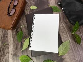 Still life photography blank notebook on wooden table with a cup of coffee, plant, leaf on table photo